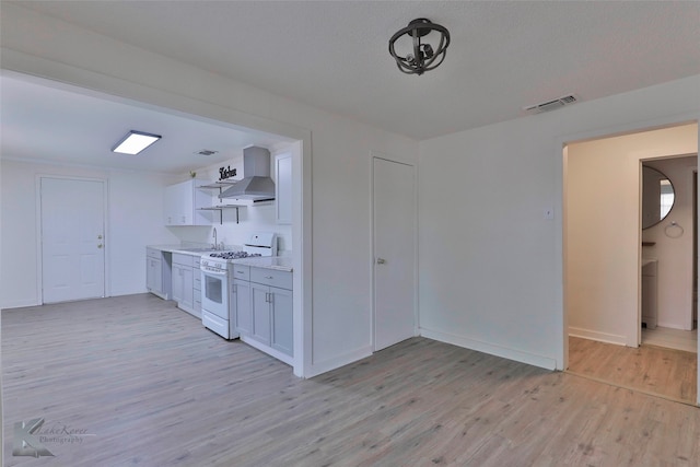 kitchen with wall chimney range hood, white cabinetry, white range with gas cooktop, and light wood-type flooring