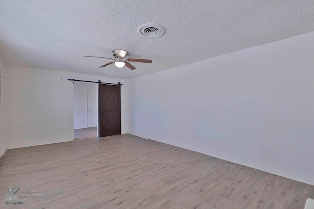 spare room featuring ceiling fan, a barn door, light hardwood / wood-style floors, and a textured ceiling