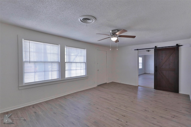 empty room with a barn door, a textured ceiling, wood-type flooring, and ceiling fan