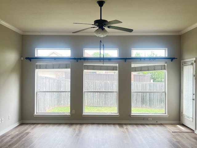 empty room with a healthy amount of sunlight, ceiling fan, ornamental molding, and hardwood / wood-style flooring