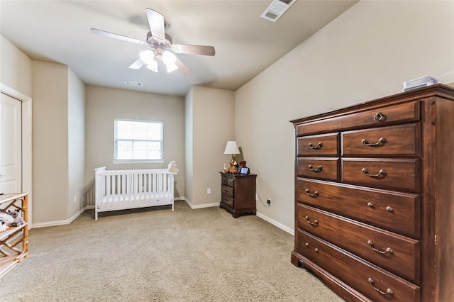 bedroom with a crib, ceiling fan, and light colored carpet