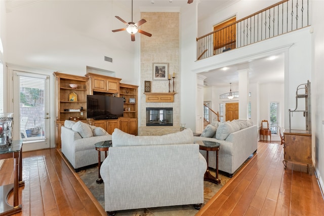 living room featuring hardwood / wood-style flooring, a fireplace, a high ceiling, ornate columns, and ceiling fan