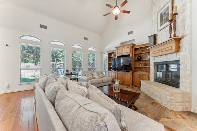 living room featuring light wood-type flooring, ceiling fan, a stone fireplace, high vaulted ceiling, and ornamental molding