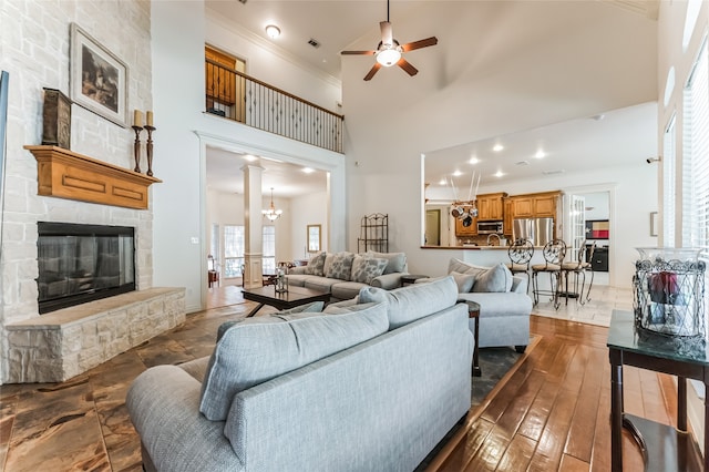 living room with wood-type flooring, a fireplace, ceiling fan with notable chandelier, crown molding, and a towering ceiling