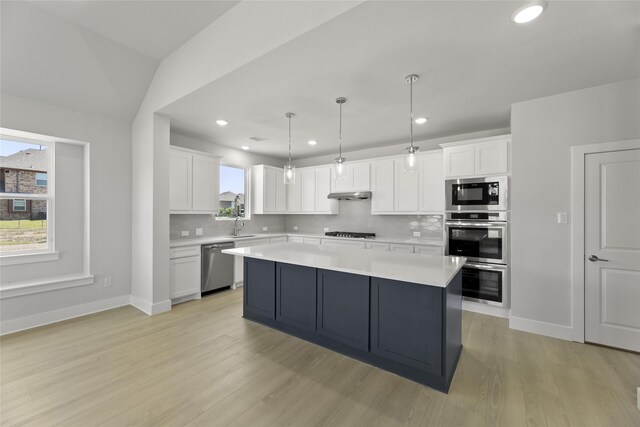 kitchen with decorative backsplash, decorative light fixtures, light wood-type flooring, and stainless steel appliances