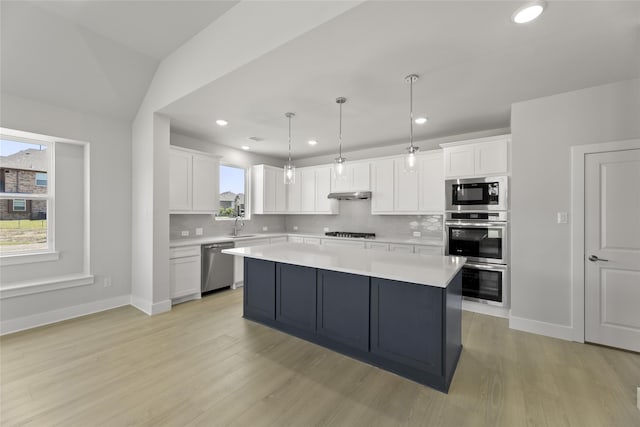 kitchen featuring white cabinetry, a center island, hanging light fixtures, appliances with stainless steel finishes, and backsplash