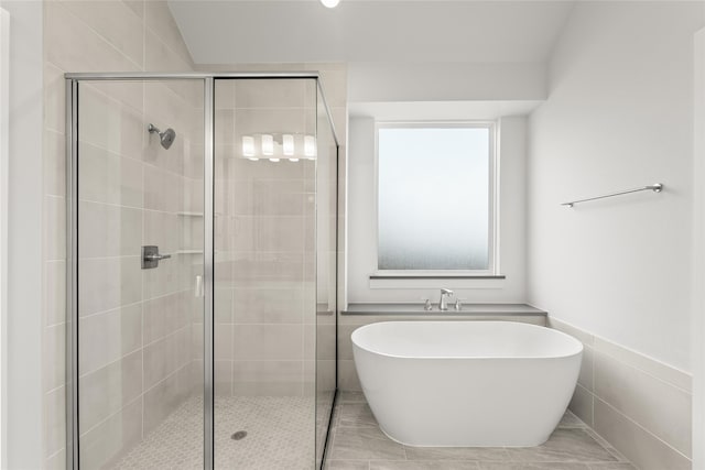 bathroom with independent shower and bath, tile patterned flooring, and tile walls