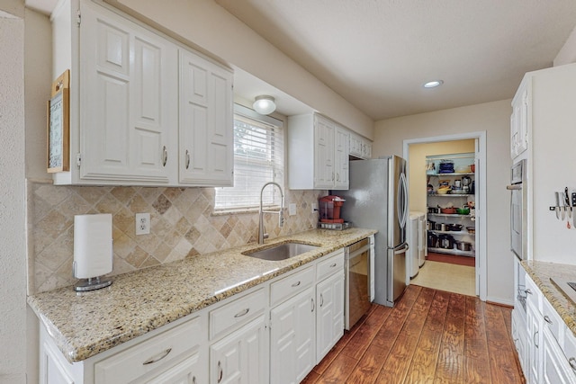 kitchen with white cabinets, sink, light stone counters, appliances with stainless steel finishes, and dark hardwood / wood-style flooring