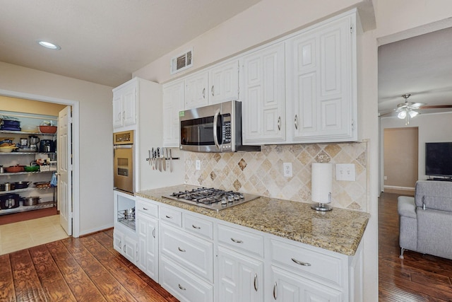 kitchen featuring ceiling fan, dark wood-type flooring, decorative backsplash, white cabinets, and appliances with stainless steel finishes