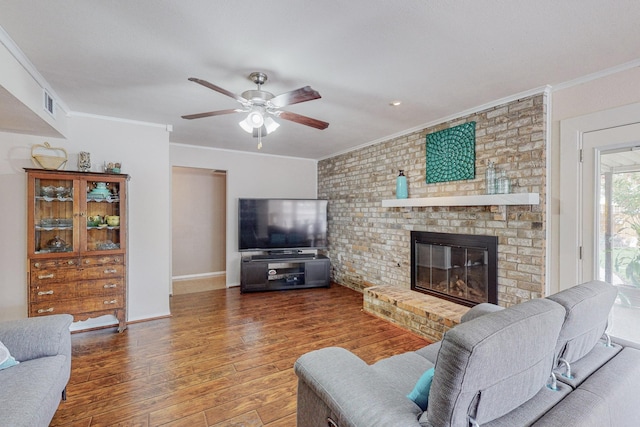 living room with ceiling fan, dark wood-type flooring, crown molding, and a brick fireplace