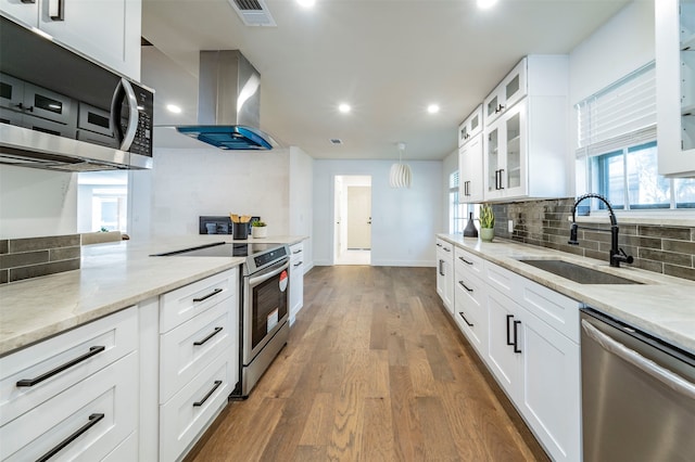 kitchen featuring stainless steel appliances, white cabinets, island exhaust hood, hardwood / wood-style floors, and backsplash