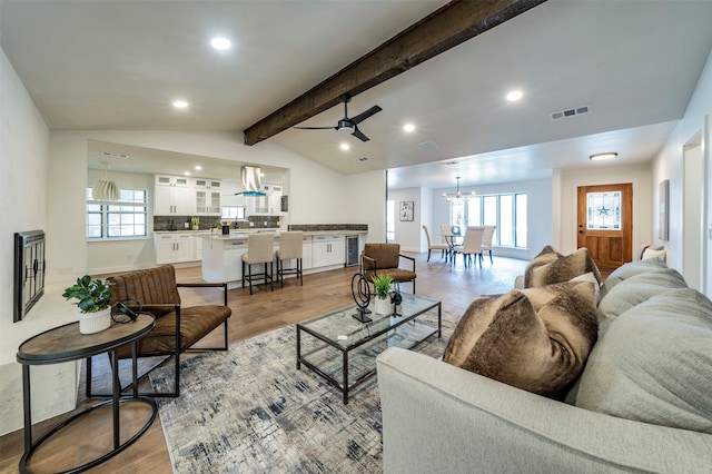 living room with lofted ceiling with beams, light wood-type flooring, and ceiling fan with notable chandelier