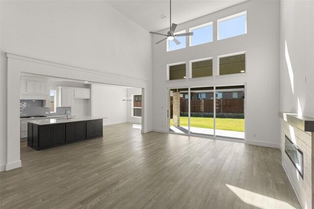 5241 Great Hollow Trl, Fort Worth, TX 76179 - unfurnished living room with a towering ceiling, a ceiling fan, a glass covered fireplace, wood finished floors, and baseboards