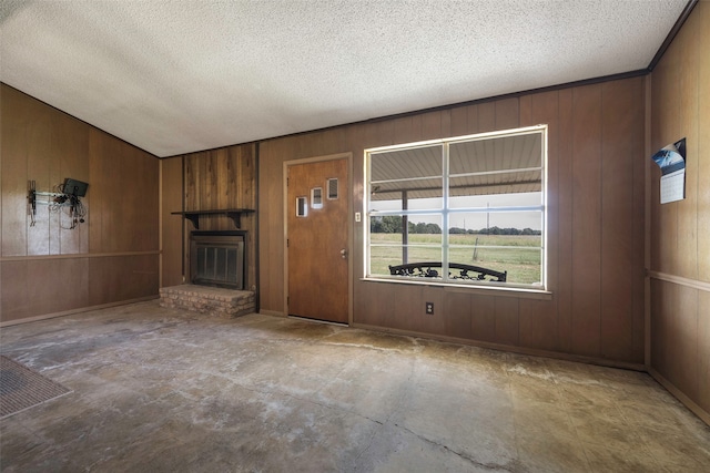 unfurnished living room with wooden walls, a textured ceiling, and a brick fireplace