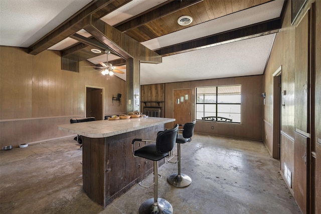 kitchen featuring a textured ceiling, concrete floors, wood walls, a breakfast bar, and ceiling fan