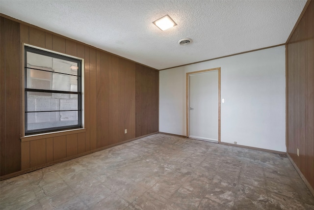 empty room featuring tile floors, a textured ceiling, and wood walls