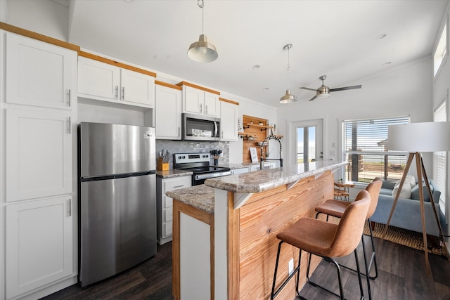 kitchen featuring light stone counters, white cabinets, ceiling fan, appliances with stainless steel finishes, and a breakfast bar area