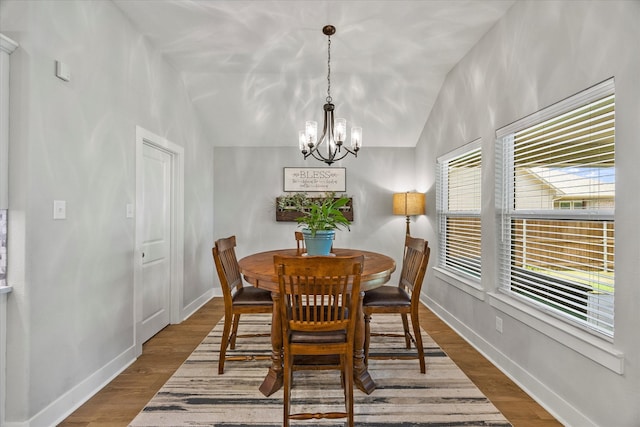 dining area with wood-type flooring, an inviting chandelier, and vaulted ceiling