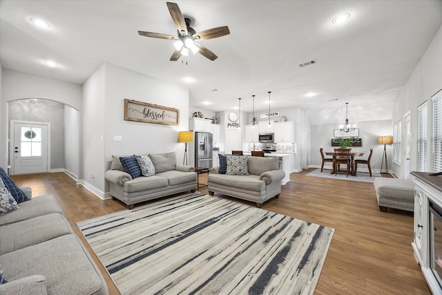 living room with ceiling fan with notable chandelier and light hardwood / wood-style floors