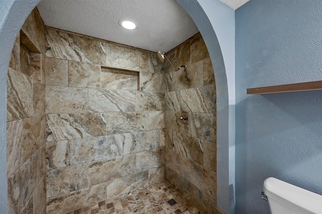 bathroom with tiled shower, toilet, and a textured ceiling