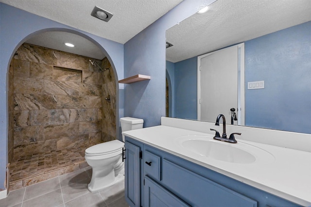 bathroom featuring tile patterned flooring, toilet, vanity, tiled shower, and a textured ceiling