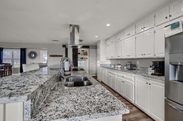 kitchen with stainless steel refrigerator with ice dispenser, a kitchen island with sink, sink, dark hardwood / wood-style floors, and white cabinetry