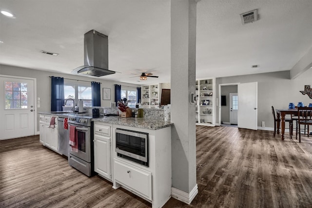 kitchen featuring light stone countertops, island range hood, stainless steel appliances, wood-type flooring, and white cabinets