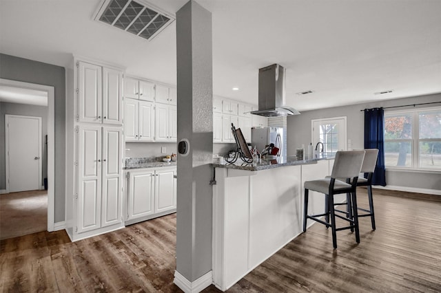 kitchen featuring stainless steel fridge, white cabinetry, hardwood / wood-style floors, and island range hood