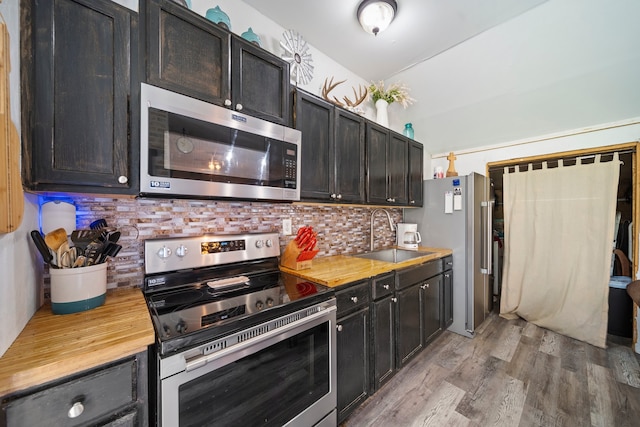 kitchen with butcher block countertops, light wood-type flooring, decorative backsplash, stainless steel appliances, and a sink