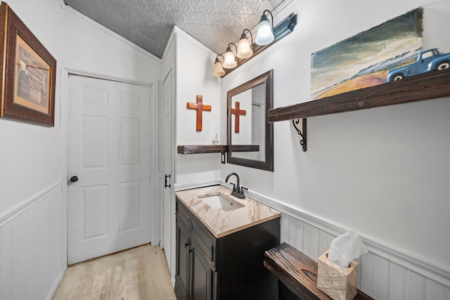 bathroom featuring a wainscoted wall, a textured ceiling, wood finished floors, and ornamental molding