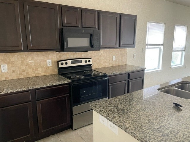 kitchen featuring light tile patterned flooring, dark brown cabinetry, light stone counters, range with electric cooktop, and decorative backsplash