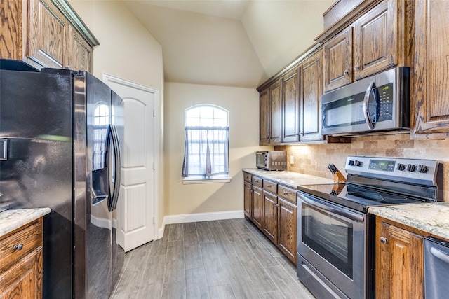 kitchen featuring vaulted ceiling, decorative backsplash, stainless steel appliances, light stone countertops, and light hardwood / wood-style flooring