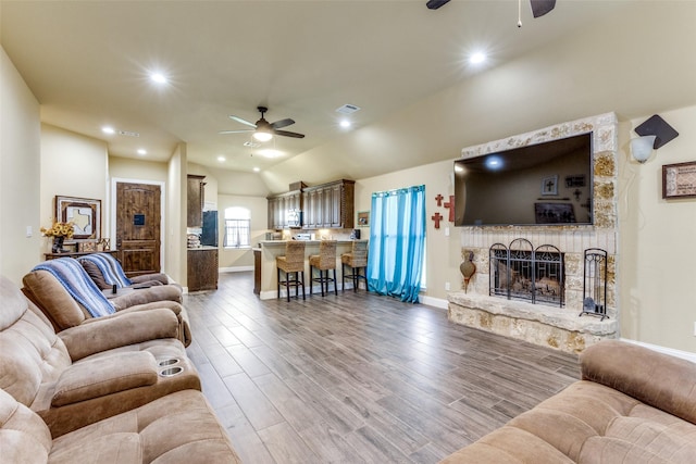 living room featuring ceiling fan, wood-type flooring, and a stone fireplace