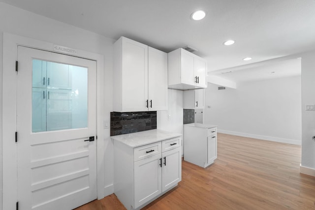 kitchen with light stone countertops, backsplash, white cabinets, and light hardwood / wood-style flooring