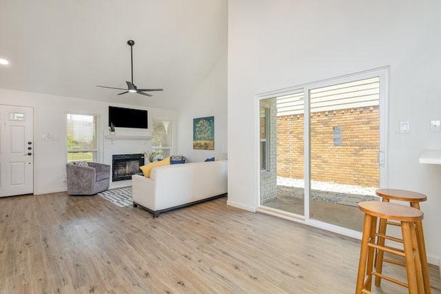 living room with ceiling fan, light wood-type flooring, and high vaulted ceiling