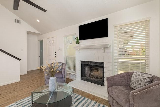 living room featuring hardwood / wood-style floors, ceiling fan, vaulted ceiling, and a brick fireplace