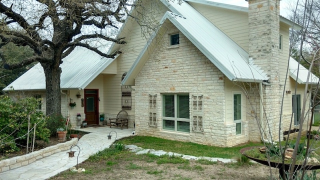 rear view of house with stone siding, a chimney, and metal roof