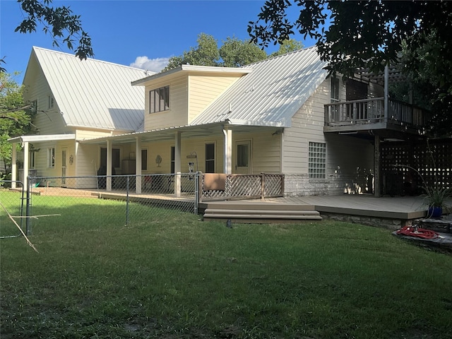 rear view of house with a lawn, fence, a wooden deck, and metal roof