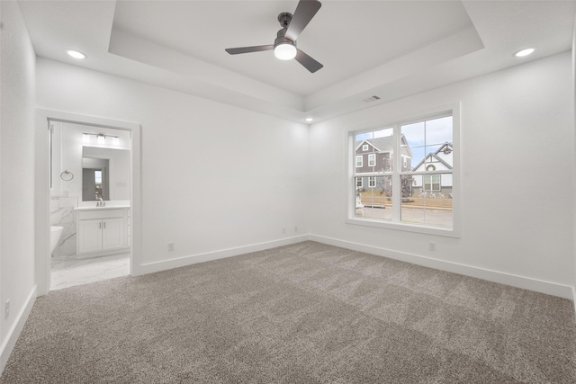 carpeted empty room with ceiling fan, a raised ceiling, and sink