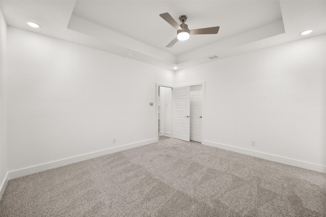 spare room with a raised ceiling, ceiling fan, and carpet floors