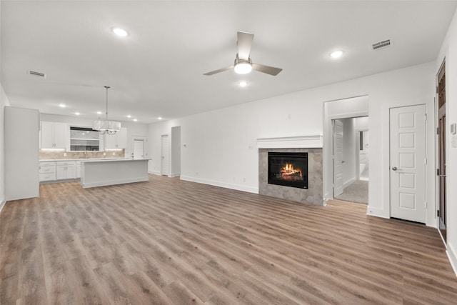 unfurnished living room featuring a tile fireplace, ceiling fan with notable chandelier, light hardwood / wood-style flooring, and sink