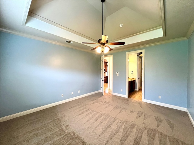 unfurnished bedroom with a walk in closet, light colored carpet, ornamental molding, a tray ceiling, and ceiling fan