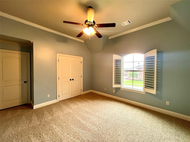 unfurnished bedroom featuring lofted ceiling, crown molding, a closet, ceiling fan, and carpet