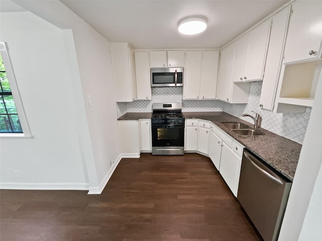 kitchen featuring dark wood-type flooring, stainless steel appliances, white cabinetry, dark stone counters, and sink