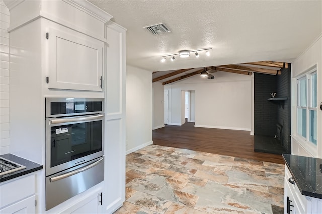 kitchen with dark stone countertops, lofted ceiling with beams, a textured ceiling, white cabinets, and oven