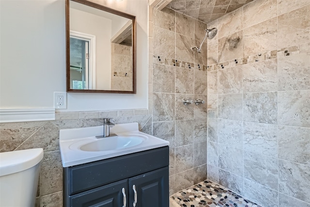 bathroom with tile walls, vanity, toilet, and a tile shower