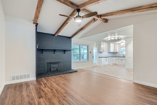 unfurnished living room featuring vaulted ceiling with beams, a healthy amount of sunlight, hardwood / wood-style floors, and ceiling fan