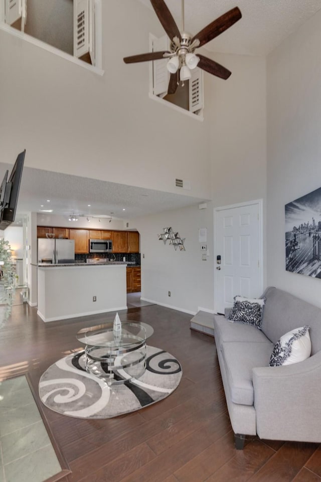 living room featuring dark wood-type flooring, ceiling fan, and a high ceiling