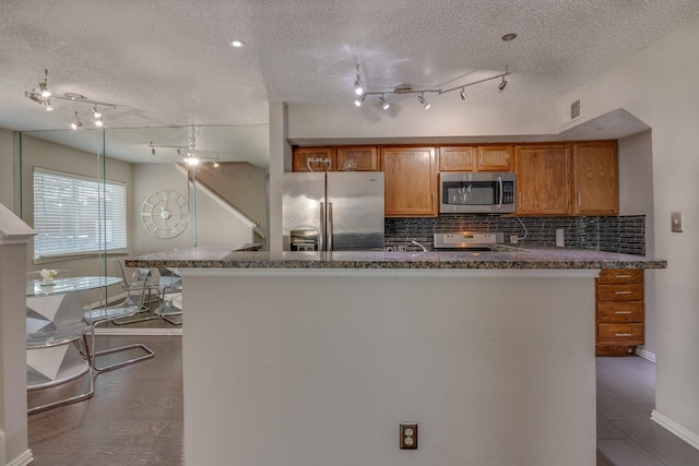 kitchen featuring tasteful backsplash, a textured ceiling, dark hardwood / wood-style flooring, kitchen peninsula, and stainless steel appliances