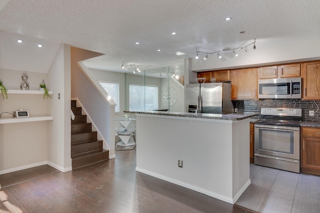 kitchen with appliances with stainless steel finishes, a center island, tasteful backsplash, a textured ceiling, and dark stone counters